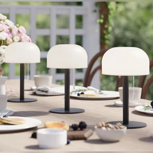 Tre sorte LED bordlamper på et dækket havebord med kager, bær og blomster